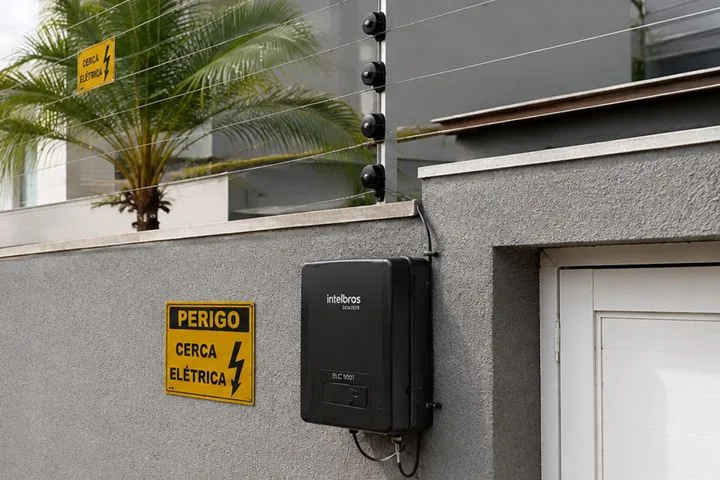 Central eletrificadora de cerca elétrica instalada no muro, ao lado da placa de advertência