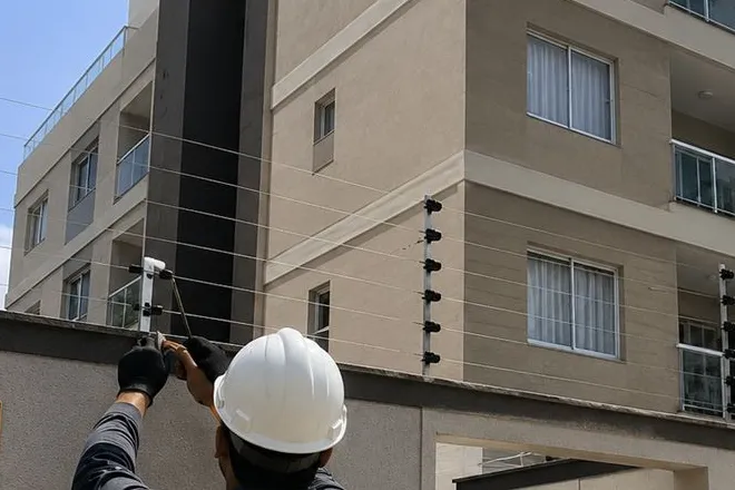 Técnico da Fênix Protege de capacete ajustando os fios da cerca elétrica no alto do muro de um prédio